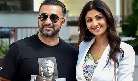 Image of businessman Raj Kundra and his wife Shilpa Shetty. Raj is wearing a black t shirt with black shades whereas Shilpa is wearing a white suit (western).