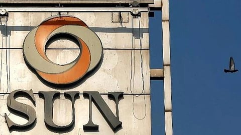 A building sign with the "Sun Pharma" logo and text prominently displayed against a blue sky background. A bird is captured flying nearby to the right.