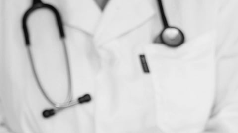 A doctor in a white coat with a stethoscope puts on latex gloves. The image conveys readiness and professionalism in a medical setting.