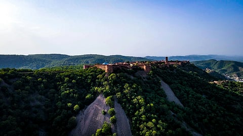 Aerial view of a historic fort perched on a lush, green hill under a clear blue sky.