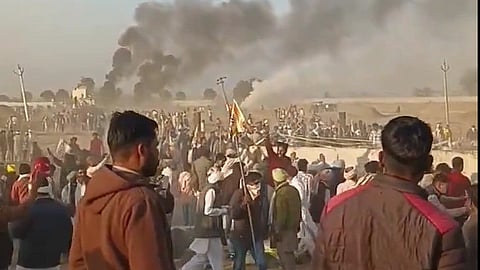 A screenshot from a video of the farmers' agitation in Rajasthan. many people can bee seen gathered near a wall, with black smoke rising in the background.