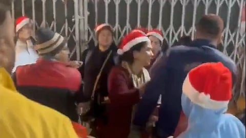 A screenshot of a video showing 2-3 men shotuing and ushering women and children wearing Santa hats out of a market.