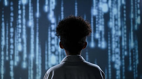A person with curly hair in a white shirt looks at a wall displaying digital code streams.