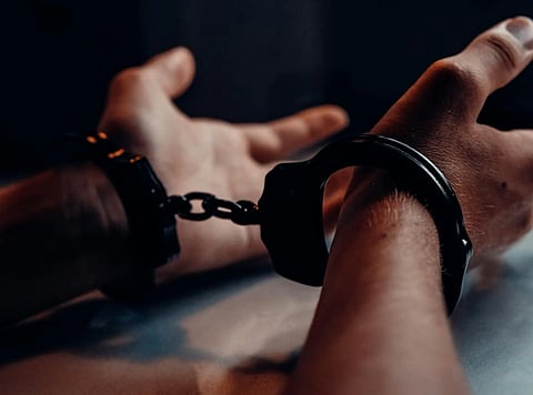 A close-up of hands in handcuffs resting on a table, dim lighting creates a tense atmosphere, suggesting confinement and restraint.
