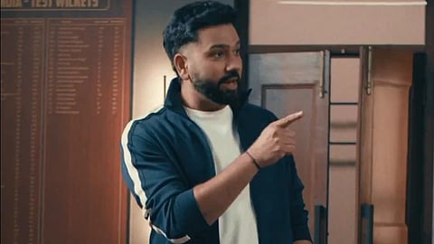 Indian Cricketer Rohit Sharma in a casual navy tracksuit gestures confidently with a smile in a room with a cricket record board. It is a snapshot of the scene from the Netflix Promo of Stranger's Things.