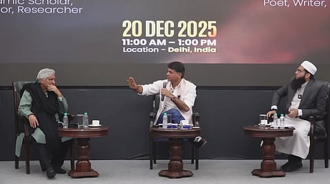 The image depicts Javed Akhtar, Saurabh Dwivedi and Mufti Shamail Nadwi, sitting from left to right. They are engaged in the debate, while Saurabh Dwivedi is addressing something in a mic. The poster behind shows the date, time and location (20 DEC 2025, 11 AM - 1 PM, Delhi, India).