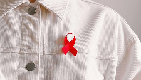 Person wearing a white shirt adorned with a bright red awareness ribbon on the chest, symbolizing support and solidarity for AIDS awareness.
