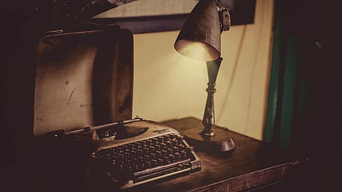 Vintage typewriter and a dimly lit lamp on a wooden desk, conveying a nostalgic and moody ambiance.
