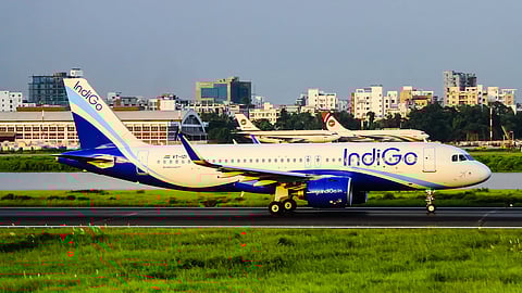An IndiGo plane on the runway, with two other planes in the background and buildings in the distance.