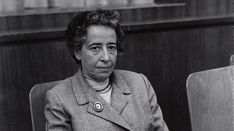 Hannah Arendt in black-and-white, sitting on a chair and staring into the camera.