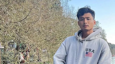 Anjel Chakma leans a gainst a railing in front of a lake while wearing a hoodie.