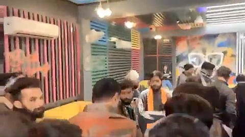 The footage of the cafe crowded by the group of men who barged into the birthday celebration, launching attacks and assaulting the guests. The cafe is crowded with colorful striped walls and graffiti. People are gathered closely, some wearing coats.