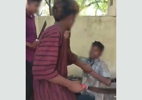 The image depicts the 2 attackers assaulting Suraj, while he is on the ground. The faces are blurred. The victim is wearing a white printed shirt, while one of the attacker is wearing a red and black striped shirt, and the other attacker is wearing a mehroon plain shirt.