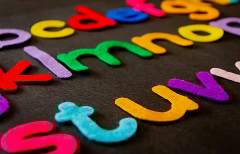 Colorful felt letters scattered on a dark background. Letters are in vibrant shades of red, yellow, green, blue, purple, and orange, creating a playful tone.