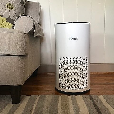 An air purifier in a living room next to a couch. 