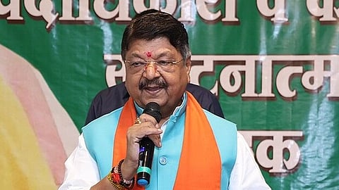 Minister Vijayvargiya in a political gathering adressing the people he is holding mic wearing an indian kurta and half coat with a orange gamcha