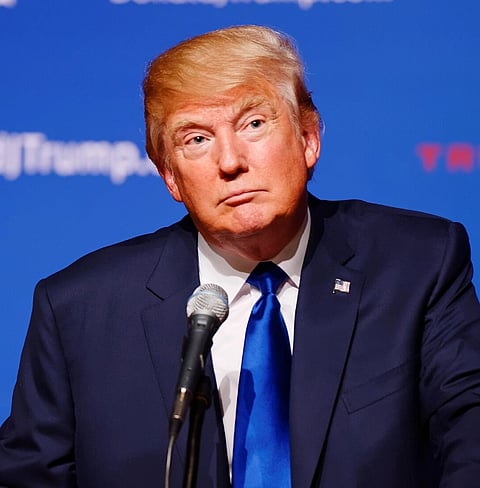 Image of President Donald Trump speaking in front of a mic in his dark blue suit and blue tie. He is speaking in front of the New Hampshire Town Hall at Pinkerton Academy, August 19th, 2015