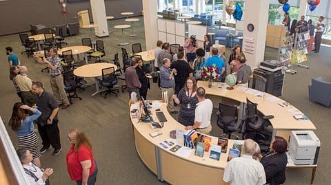 Spacious library with groups of people chatting around a large, curved information desk with books and materials