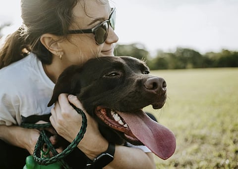 A woman holds her pet dog, in a field.