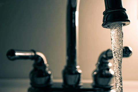 Close-up of a modern chrome faucet with water flowing steadily from the spout, captured in warm lighting, conveying a sense of cleanliness and freshness.