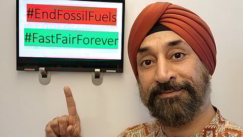 Harjeet Singh pointing at a sign reading #EndFossilFuels and #FastFairForever