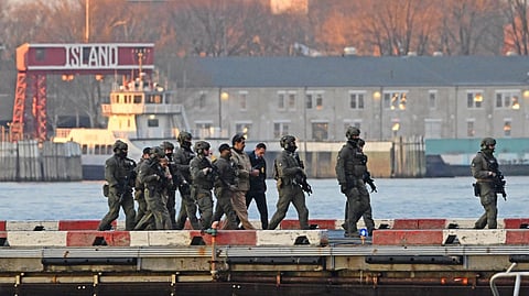 A group of armed, uniformed officers escort Venezuelan President Maduro and his wife across a pier. The backdrop includes water, a docked boat, and industrial buildings, creating a tense atmosphere.