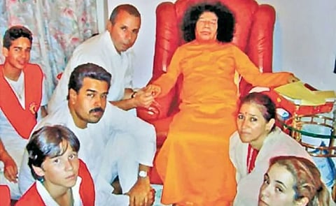 In the image Sathya Sai baba is shown sitting in sofa with other people sitting on ground within the people is President of Venezuela Maduro and his wife