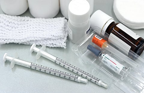Medical supplies on a surface, including syringes, vials, bottles, gauze, and cotton pads. The scene conveys a clinical and sterile tone.