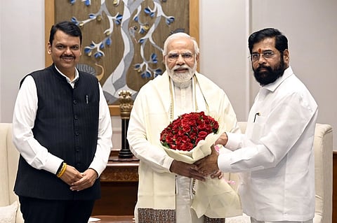 Narendra Modi poses with Eknath Shinde and Devendra Fadnavis. Shinde is handing him a bouquet of roses.