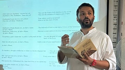 Prof. Ali Khan Mahmudabad reading from a book in font of a projected screen.