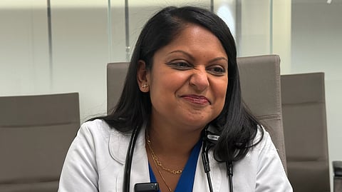 Indian American physician Dr Tina Shah smiling in a white lab coat with a stethoscope, sitting indoors in a modern office setup.
