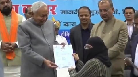 A screenshot from a viral video shows Nitish Kumar handing a certificate to a woman in a hijab, felicitating her appointment as a doctor. He later proceeds to pull down her hijab, prompting widespread criticism.