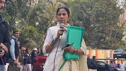 Mamata Banerjee holding mic in one hand, a green file with documents and a phone in the other.
