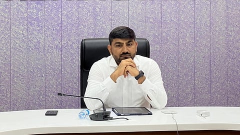 IAS Rajendrakumar Patel sitting at a white desk with his hands together.