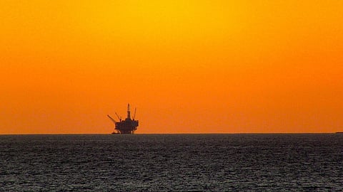 Silhouette of an oil drilling platform off the coast of Santa Barbara, CA, in front of an orange sky.
