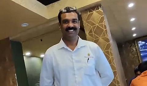 Shrikant KG Smiling in white shirt with glasses on his head stands in a warmly lit restaurant, featuring geometric wall patterns, conveying a friendly atmosphere.
