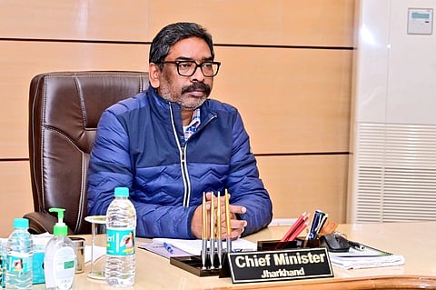 The image is a picture of Jharkhand CM Hemant Soren, sitting in his office, with his nameplate on the table