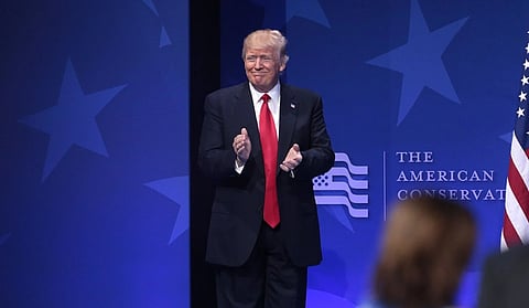 Image of President Donald trump clapping speaking at the 2017 Conservative Political Action Conference (CPAC) in National Harbor, Maryland. Behind him is a blue background with text, " the American conservative" written.