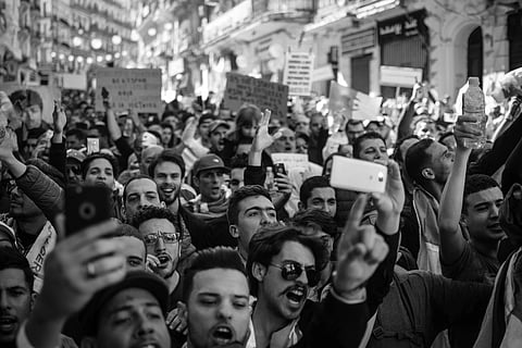 Crowd of protesters in a lively street demonstration, holding signs and phones, conveying unity and determination in a bustling urban setting. Black and white.