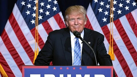 Image of US president Donald Trump speaking at an immigration policy speech in Phoenix, Arizona. in the image he standing in front of a podium which says 'Trump Fence'. There are US national flags behind him. 
