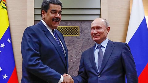 Russian President Vladimir Putin shaking hands with Venezuelan leader Nicolas Maduro. Both are dressed in blue suit and are smiling.