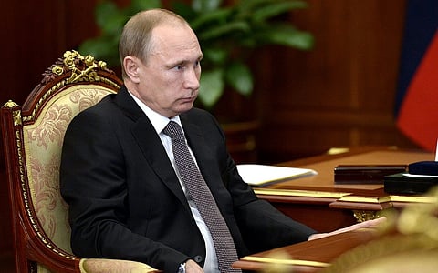 Image of Russian President Vladimir Putin sitting in a chair. the camera is placed on his right and  a table is placed in front of him.