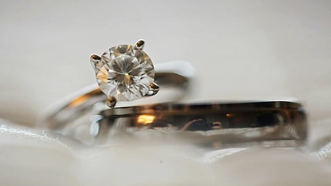 Close-up of an elegant diamond engagement ring resting against a silver wedding band on a soft, blurred background