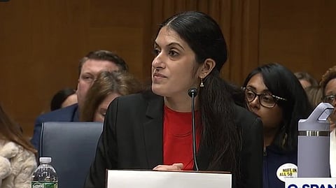 Indian-American obstetrician-gynaecologist Dr Nisha Verma in a red shirt and black blazer speaks into a microphone at a formal hearing. The setting conveys seriousness, with attendees focused.