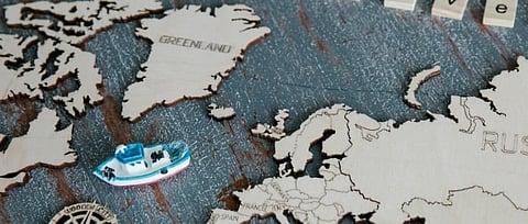 Wooden world map with a miniature boat and compass on top. The word "travel" is spelled out with letter tiles, conveying adventure and exploration.