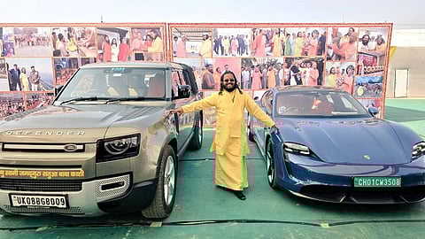 Satua Baba stands between two of his cars, a Porshce and a Land Rover, while wearing Ray Bans.