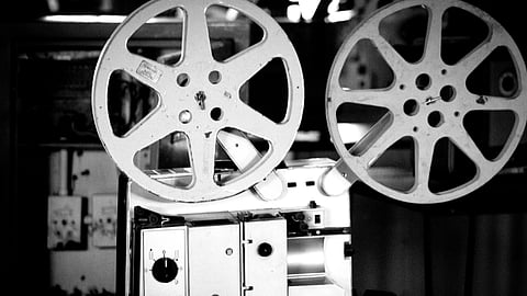 Black and white image of a vintage film projector with two large reels, conveying a nostalgic and cinematic atmosphere.