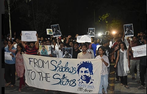 A protest organised by AIOBCSA against the institutional murder of Rohith Vemula. Many people are marching holding up placards, the poeple leading are holding a banner with Vemula's face, reading "From shadows to the Stars".