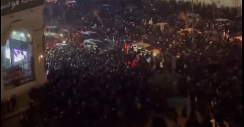 Overhead view of a large, dense crowd gathered in a city street at night, with dim lighting. The scene is busy and conveys a sense of urgency and anticipation.