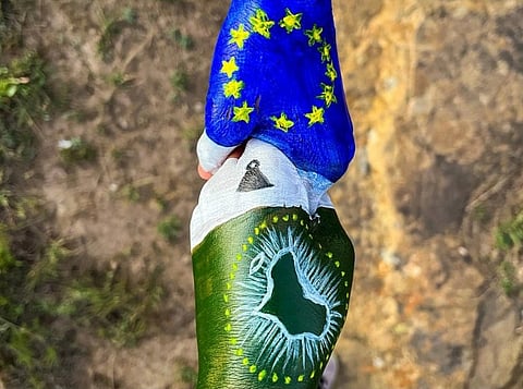 Two people shaking hands, one is painted with the EU flag, the other with the AU flag.